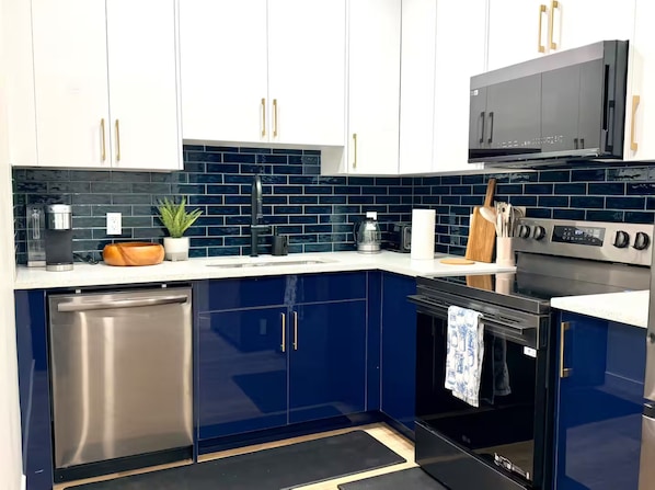A modern kitchen with dark blue cabinets, stainless steel appliances, and a black countertop.
