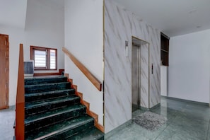 Eine Treppe mit Marmorwänden und einem hölzernen Geländer, die zu einem Aufzug führt.