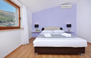 Une chambre d’hôtel comprenant un lit, deux tables de chevet, une fenêtre avec des rideaux et un appareil de climatisation.