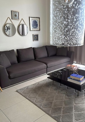 A modern living room with a dark grey sofa, a black coffee table with books and glasses, and a decorative wall with framed pictures. - Modern 1-bedroom apartment with AC in serene Doral (Doral)