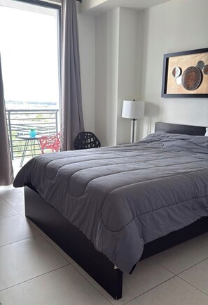 Una habitación de hotel con una cama grande, un balcón con una silla y un cuadro en la pared.