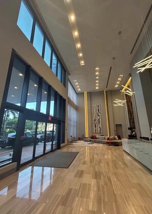 A spacious lobby with large windows, a reception desk, and a modern light fixture. - Modern 1-bedroom apartment with AC in serene Doral (Doral)