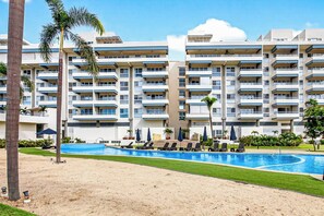 Ein mehrstöckiges Hotel mit Swimmingpool, Liegestühlen und Palmen.