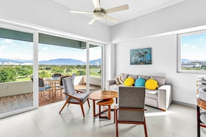 Ein modernes Wohnzimmer mit einer Couch, Sesseln, einem Esstisch und einem großen Fenster mit Blick auf die Stadt.
