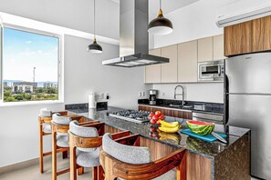Eine moderne Küche mit einer zentralen Kochinsel, Barhocker, Edelstahlgeräten und Blick auf die Stadt.