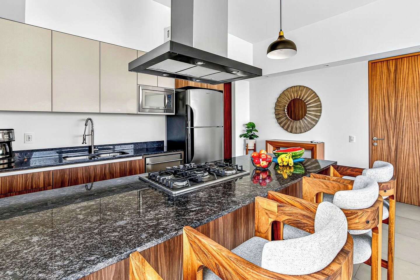 A modern kitchen with a central island, stainless steel appliances, and a wooden dining area.