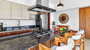 A modern kitchen with a central island, stainless steel appliances, and a wooden dining area.