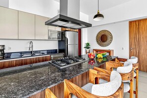 A modern kitchen with a central island, stainless steel appliances, and a wooden dining area. - ~Sunny ~Apartment • Relax Steps from the Sand (Nuevo Nayarit)