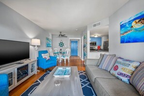 A living room with a TV, blue armchair, grey sofa, and a coffee table. - Oceanfront 2BR • Pool • Walk Beach • Sleeps 6 (Fernandina Beach)