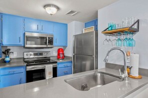 A modern kitchen with blue cabinets, stainless steel appliances, and a wine rack. - Oceanfront 2BR • Pool • Walk Beach • Sleeps 6 (Fernandina Beach)