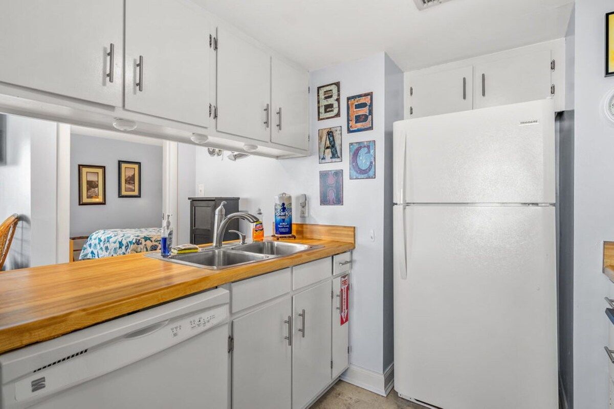 A kitchen with white cabinets, a wooden countertop, a sink, a refrigerator, and wall-mounted artwork.