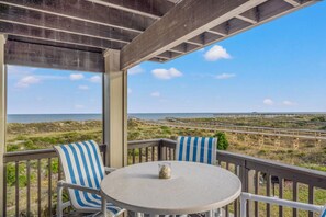 Ein überdachter Außenbereich mit Tisch und Stühlen mit Blick auf einen Strand und eine Promenade.
