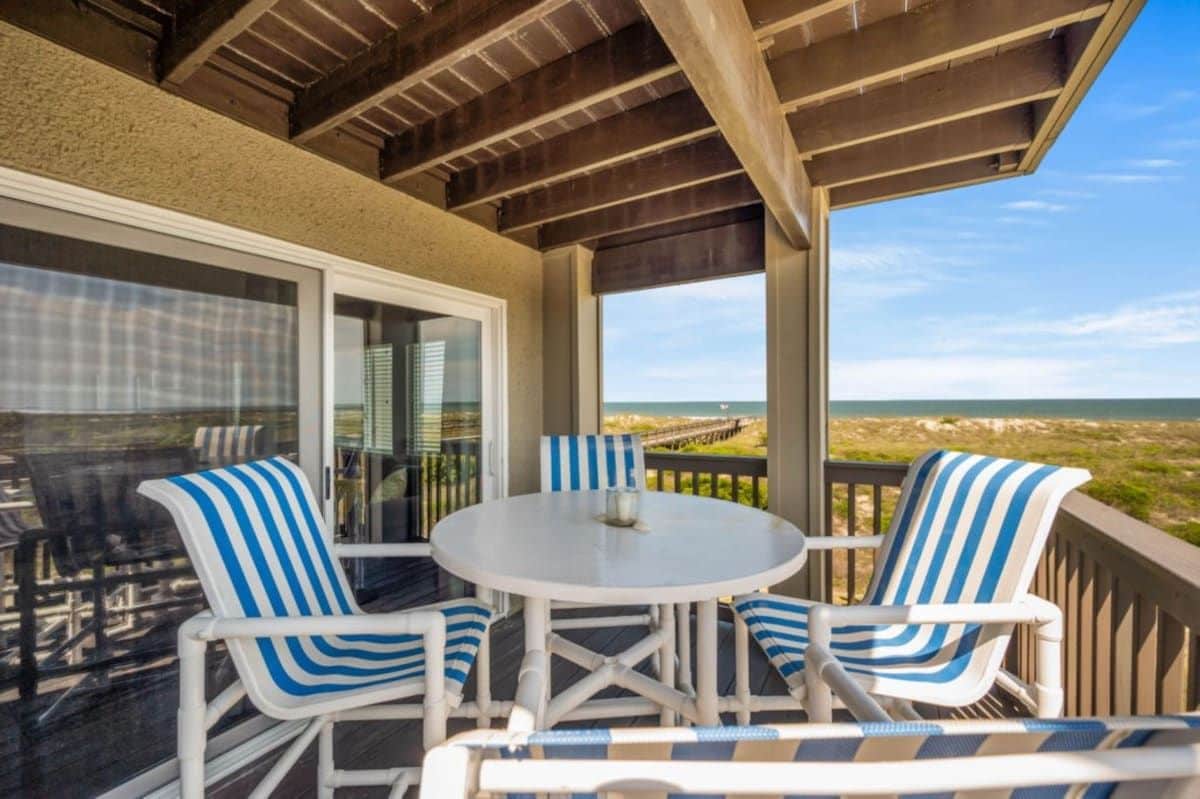 A covered outdoor seating area with a table and striped chairs, overlooking a beach.
