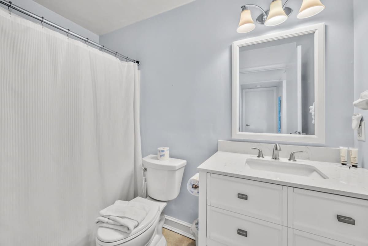 Un baño con inodoro blanco, lavamanos con espejo arriba y cortina de ducha.
