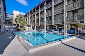 Ein mehrstöckiges Hotel mit Schwimmbad, Sitzgelegenheiten im Freien und einer Palme.