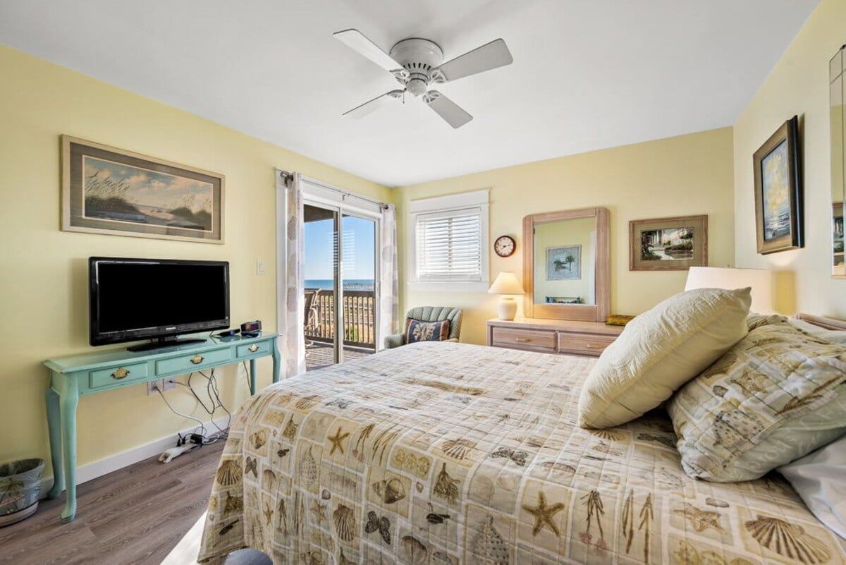 Un dormitorio con cama, televisión, ventilador de techo y vistas al exterior.