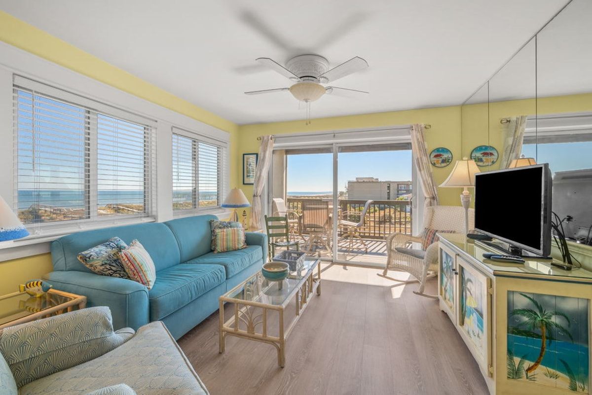 A living room with a blue sofa, a glass coffee table, a ceiling fan, and a TV.