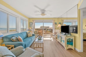 A living room with a sofa, television, and a balcony with outdoor furniture. - Best Views in Sand Dollar! Beachfront w/ Pool (Fernandina Beach)