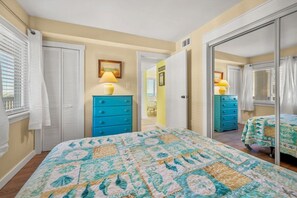 A bedroom with a bed, two blue dressers, a mirror, and a door leading to another room. - Best Views in Sand Dollar! Beachfront w/ Pool (Fernandina Beach)