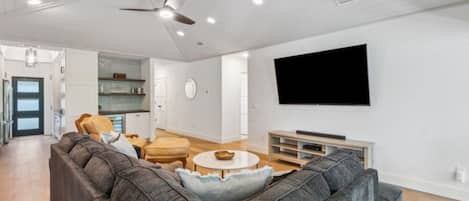 Una sala de estar moderna con un sofá seccional gris, una mesa redonda de centro y un televisor de pantalla plana montado en la pared.