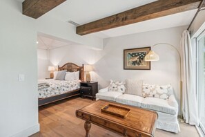 Quarto com cama, mesas de cabeceira, sofá, mesa de centro e janela com cortinas.