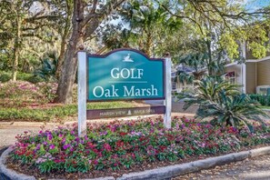 A sign for 'Golf Oak Marsh' with a 'Marsh View Bar & Grill' below it, surrounded by a flower bed and trees. - Omni Amelia Island 2BR Lagoon Villa | Walk to Beach | Sleeps 4 (Fernandina Beach)