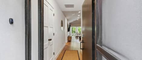A hallway with a doormat, a door, and a view into a room with a window.