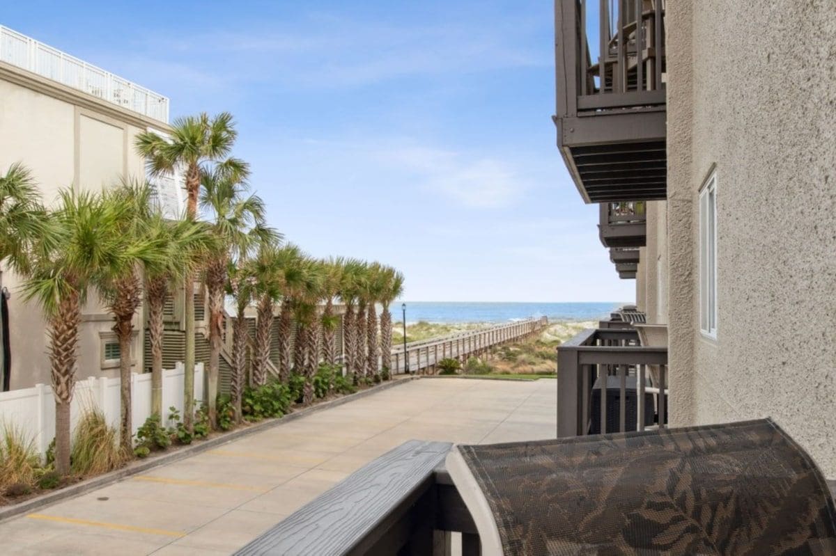 Ein Gebäude mit Balkon, ein von Palmen gesäumter Weg und Blick auf den Strand.