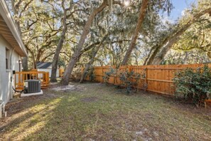 A backyard with a wooden fence, trees, and a house. - 30+ Day Coastal Cottage Near Downtown (Fernandina Beach)
