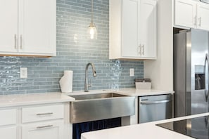 A modern kitchen with white cabinets, a stainless steel refrigerator, and a blue-tiled backsplash. - Ocean View Beach House on Amelia Island with Private Elevator and Pool (Fernandina Beach)