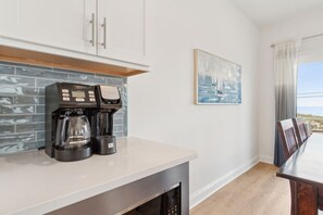 A modern kitchen with a coffee maker, a microwave, and a dishwasher. There is a dining table with chairs and a painting on the wall. - New 2025 • Ocean Views • Pool • 4BR (Fernandina Beach)