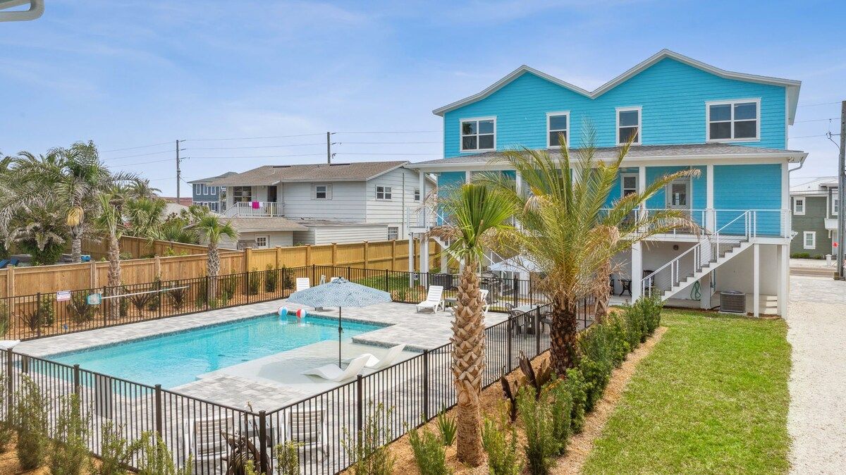 A residential area with a swimming pool, a blue house, and a fenced yard.