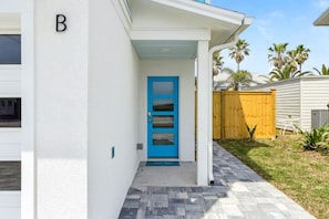 Una casa con puerta azul, cerca de madera y sendero pavimentado.