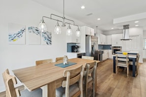 A modern kitchen with white cabinets, a wooden dining table, and pendant lights. - Brand New 4BR • Ocean Views • Pool (Fernandina Beach)