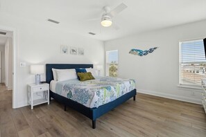 Un dormitorio con cama, mesita de noche, ventilador de techo y una obra de arte en la pared.