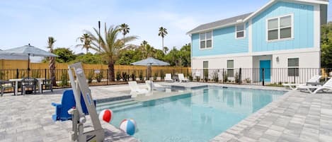 A pool area with a blue building, lounge chairs, and a slide.