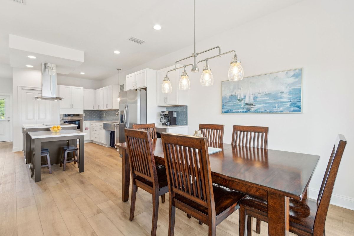 A modern kitchen with white cabinets, a dining table with wooden chairs, and pendant lighting.