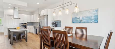 A modern kitchen with white cabinets, a dining table with wooden chairs, and pendant lighting.