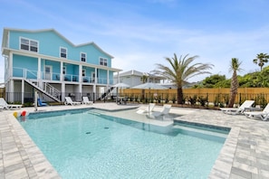 A pool area with a clear pool, lounge chairs, and a two-story building with a blue exterior. - New Oceanfront Amelia Island Beach Estate with Private Pool and Two Elevators (Fernandina Beach)
