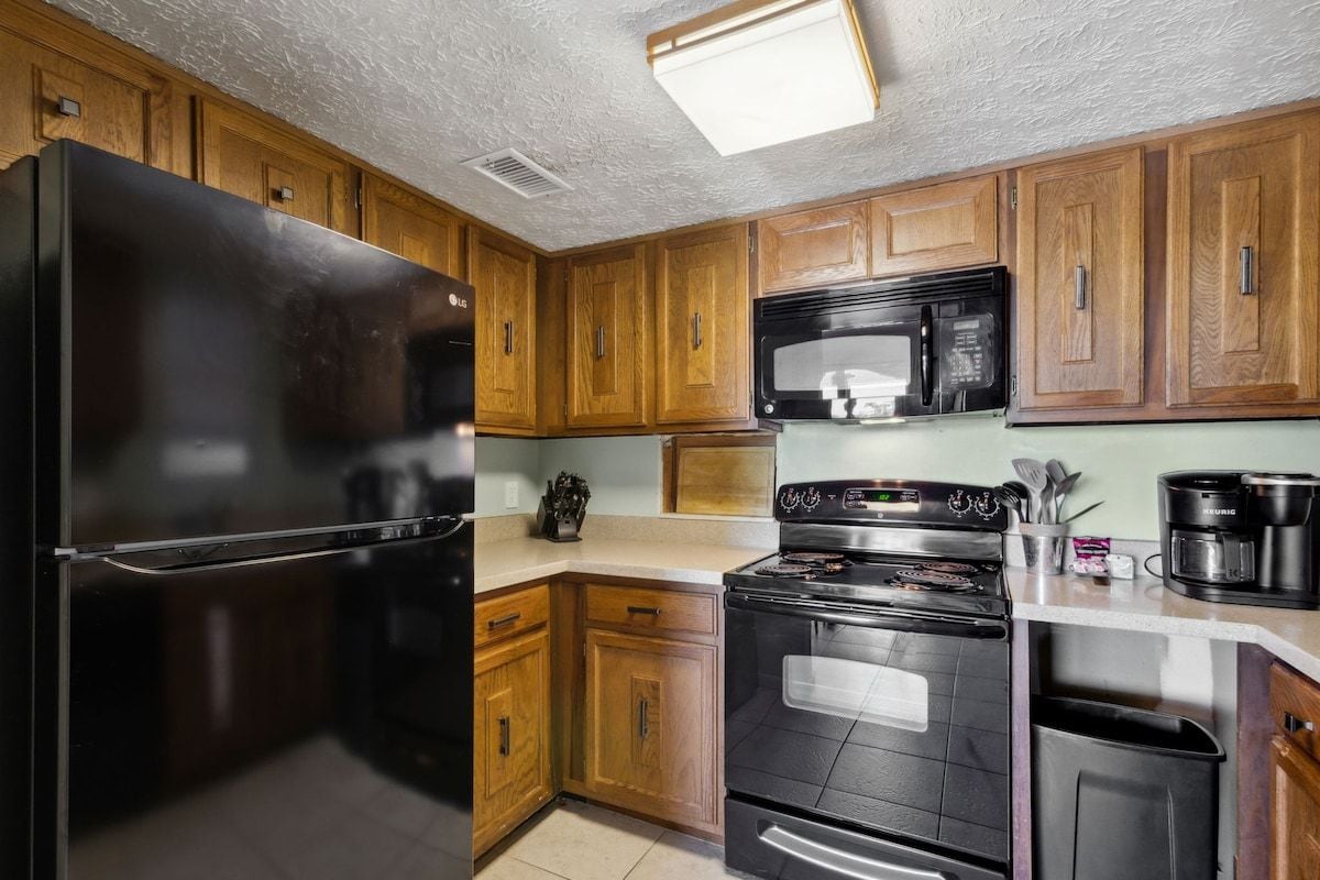 A kitchen with wooden cabinets, a black refrigerator, a microwave, a stove, and a coffee maker.