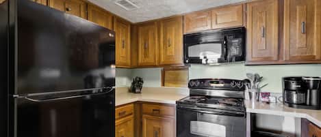 Une cuisine avec des meubles de rangement en bois, un réfrigérateur noir, un four à micro-ondes, une cuisinière et une machine à café.