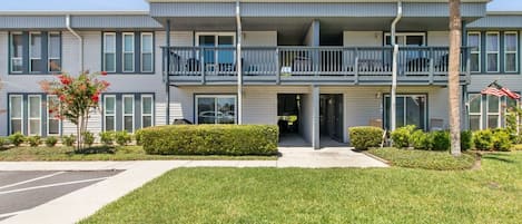 A multi-story residential building with balconies, a parking lot, and well-maintained lawns.