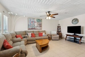 A living room with a sectional sofa, a coffee table, a television, and a ceiling fan. - Pet Friendly Fernandina Shores Condo, Walk to the Beach, Pool, Tennis (Fernandina Beach)