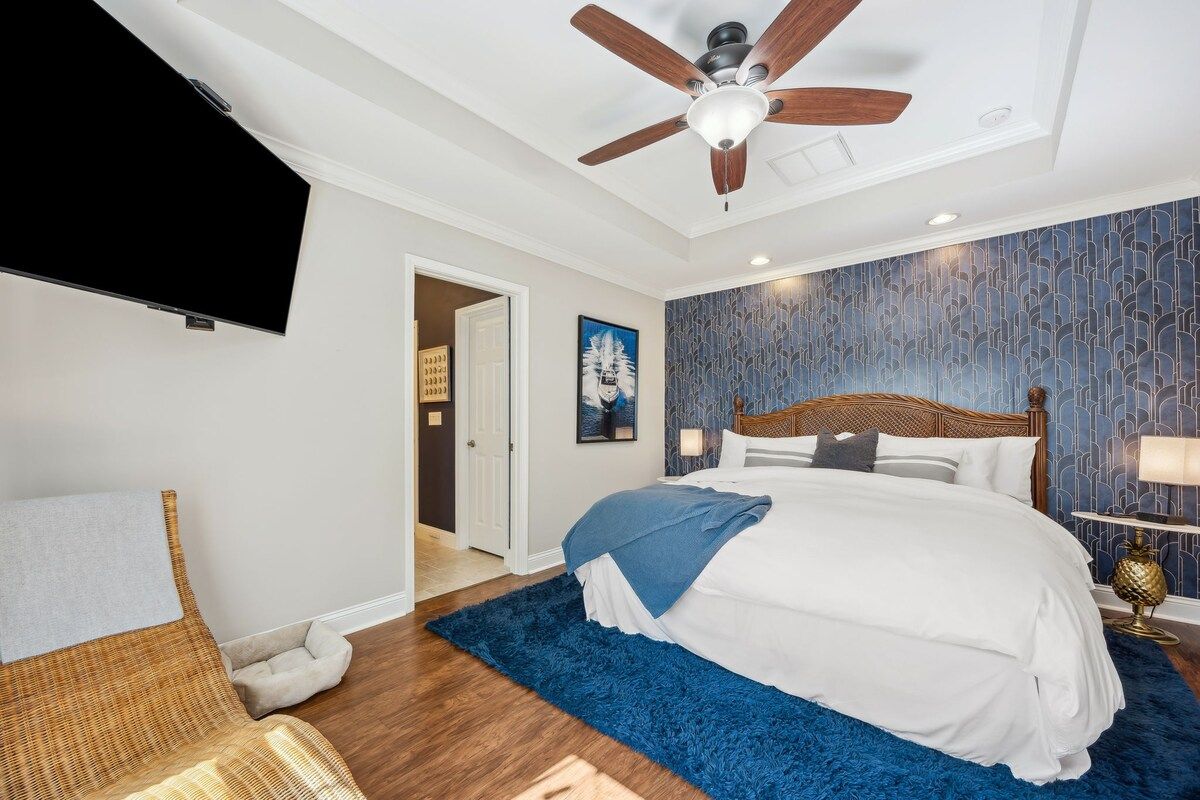 Un dormitorio con cama, ventilador de techo, televisor y pared con diseño.