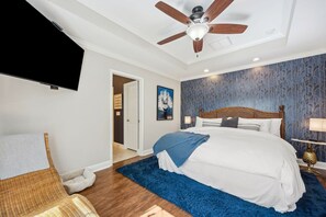 Une chambre à coucher avec un lit, un ventilateur de plafond, une télévision et un mur décoré d’un motif.