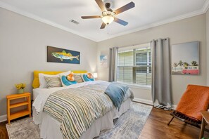 A bedroom with a bed, a ceiling fan, a window with blinds, a chair, and artwork on the walls. - The Helm on Elm beautiful 3/2 near downtown (Fernandina Beach)