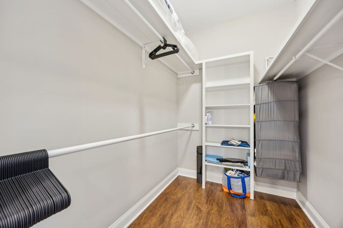 Una habitación con un estante blanco, una silla negra y una cortina gris.
