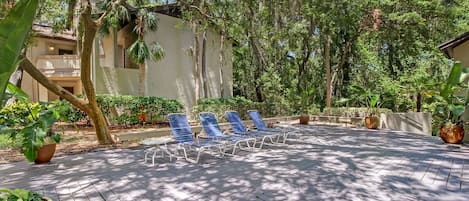 A wooden deck with lounge chairs, surrounded by trees and potted plants.