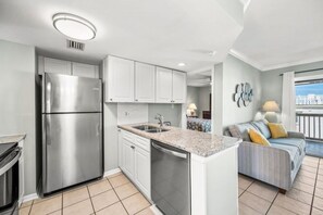 A modern kitchen with a stainless steel refrigerator, white cabinets, a built-in dishwasher, and a granite countertop. - Top Floor • Beach Access • Pool • Amelia (Fernandina Beach)