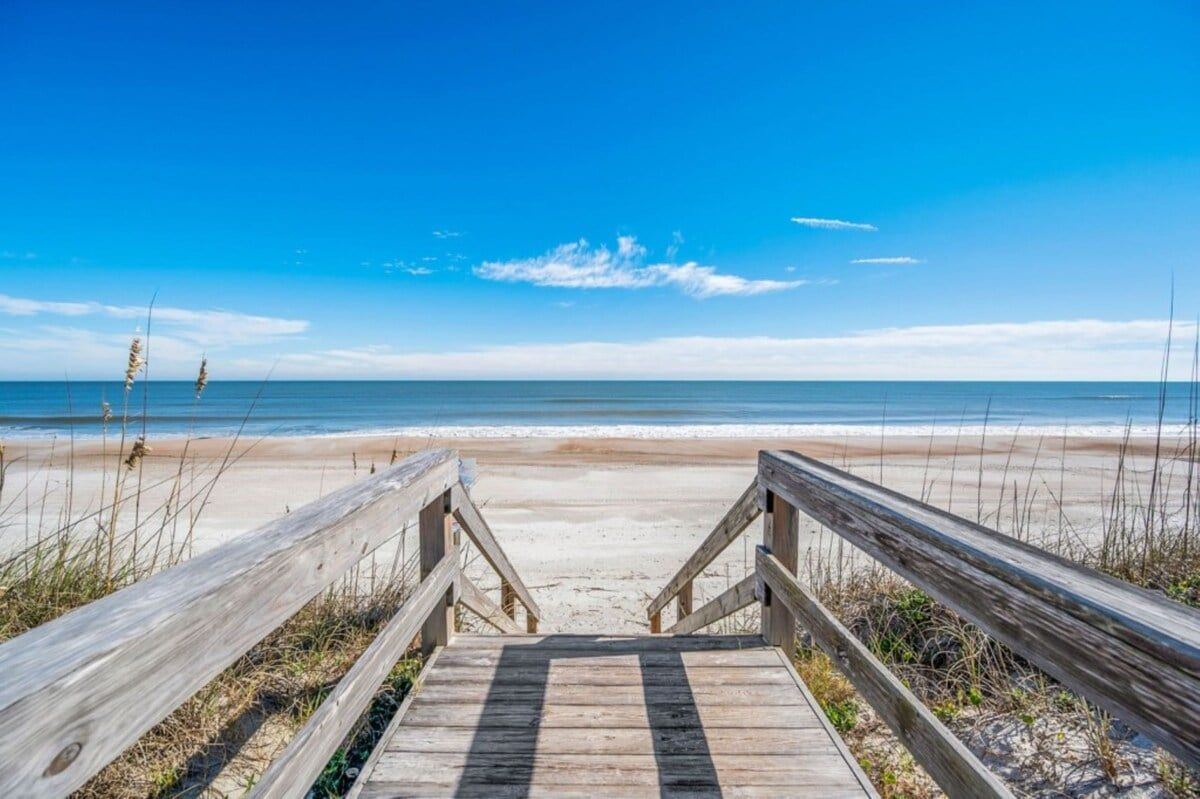 A wooden boardwalk leading to a beach with clear skies.